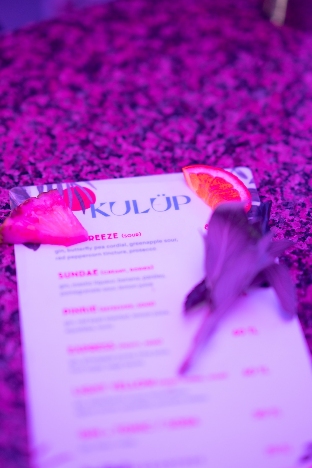 A KULÜP menu and fruit under magenta light